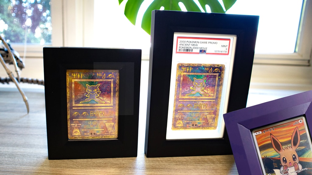 Two Ancient Mew cards, one in a PSA graded slab, inside two black collectible card frames. An Eevee card in a purple card frame is partly visible.