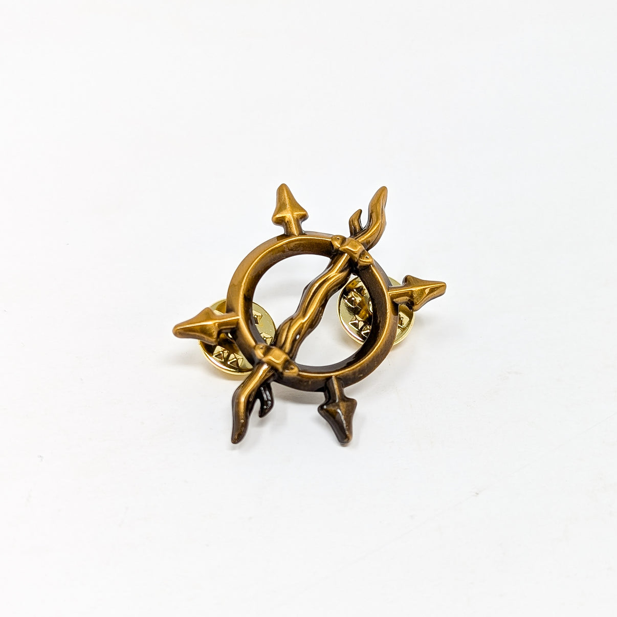 A gold-colored enamel pin with a fantasy insignia design, resembling a stylized animal or mythical creature, set against a white background.