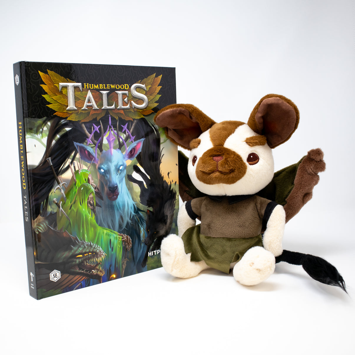 Plush toy resembling a mouse with wings next to a book titled 'Humblewood Tales' on a white background