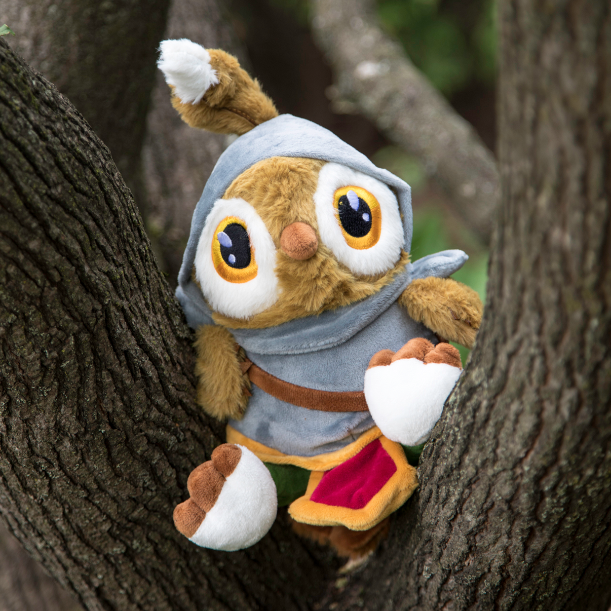 Plush toy owl character in a fantasy outfit peeking from behind tree trunks