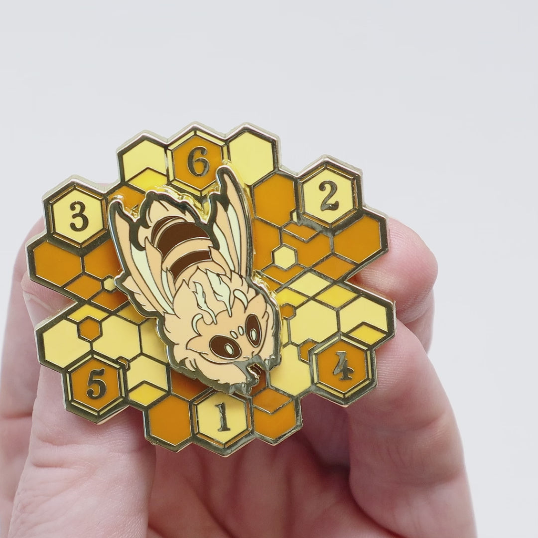 A video of an enamel pin with a bee on a hive that spins.